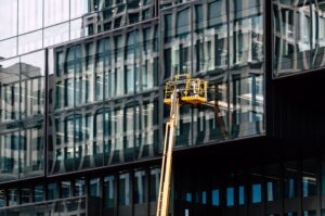 Workers on a lift cleaning windows of a modern glass building exterior.